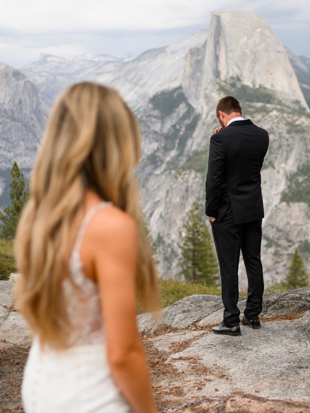 Bride in white dress looking at groom in black suit before a mountain peak