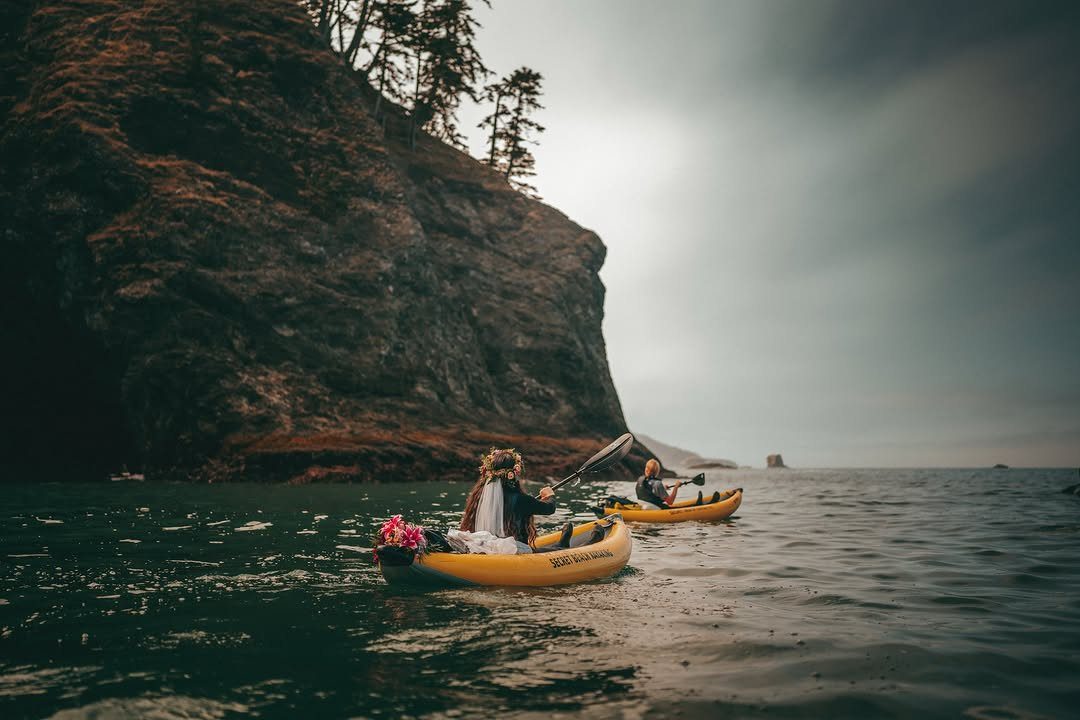 Couple in wedding attire paddling yellow kayaks near a steep rocky cliff coastline