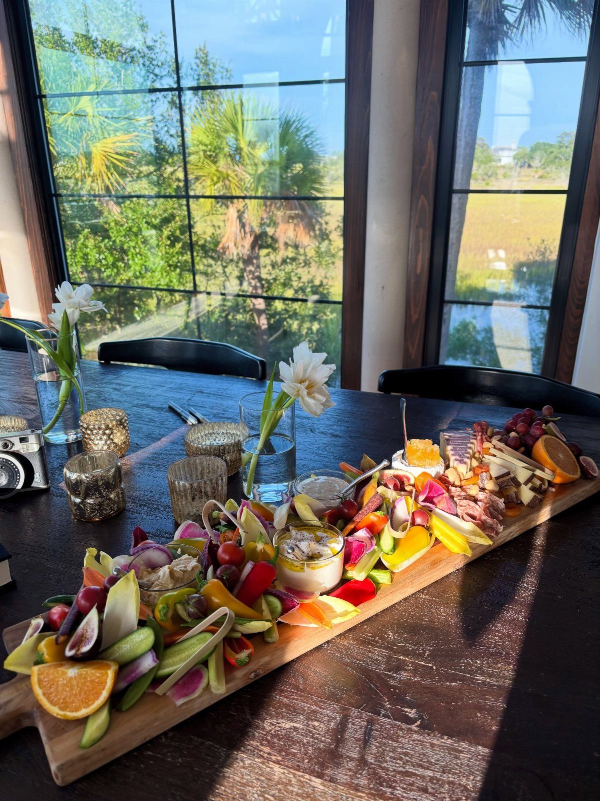 Charcuterie board with colorful fruits and cheeses on a table by a window.