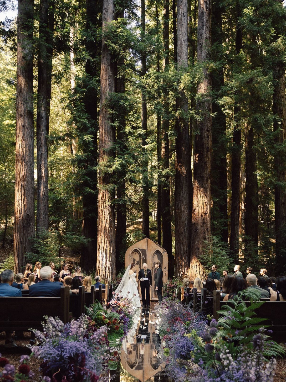 Wedding ceremony in a redwood forest with a couple under a wooden arch.