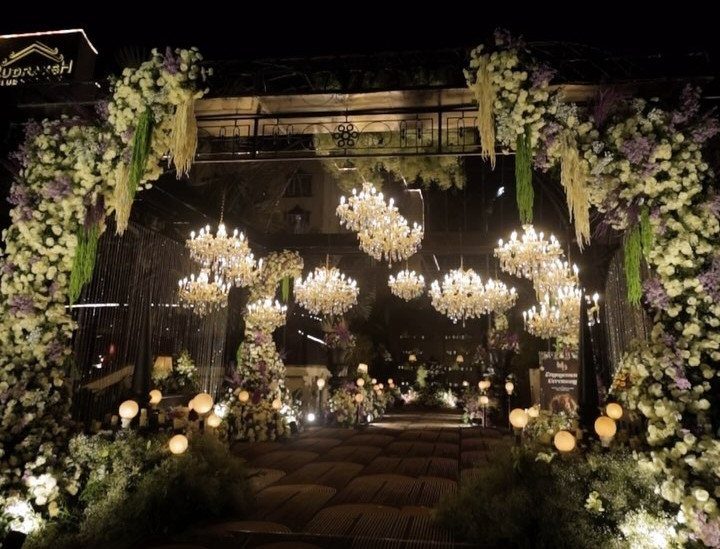 Floral archway and glowing crystal chandeliers over a wedding venue walkway at night