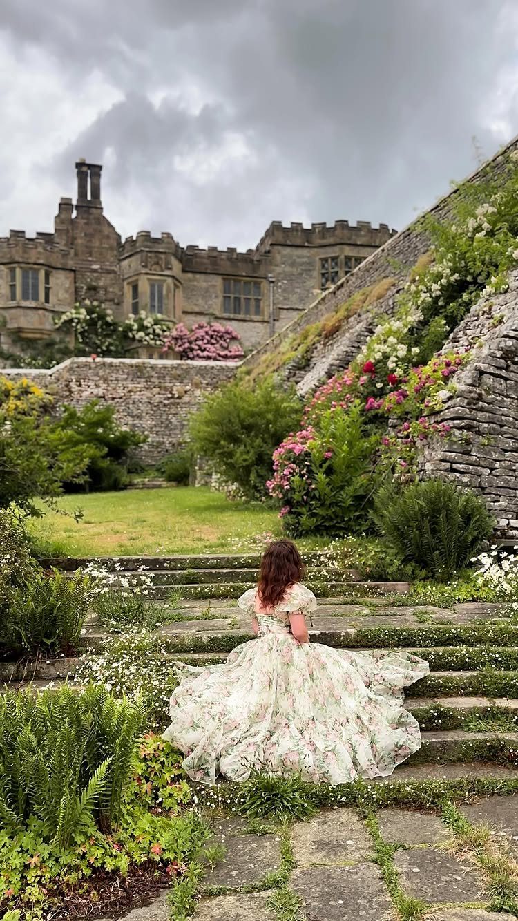 Woman in floral gown sitting on stone steps before a historic stone castle