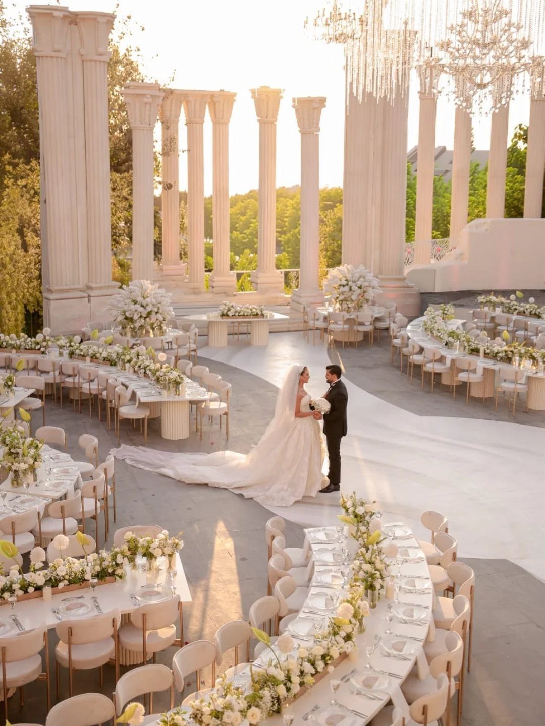 Bride and groom standing in a neoclassical outdoor venue with white columns and flowers
