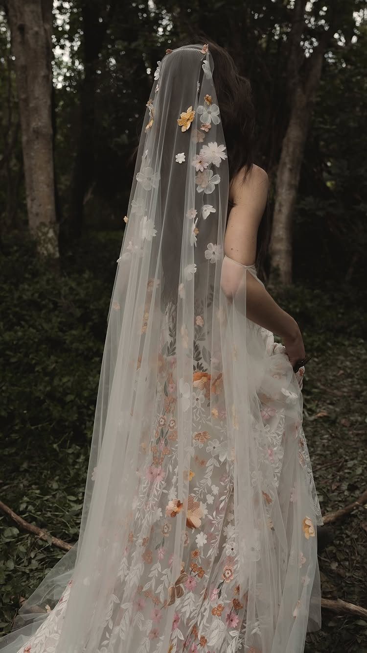 Bride in floral veil and white dress standing in a dark forest