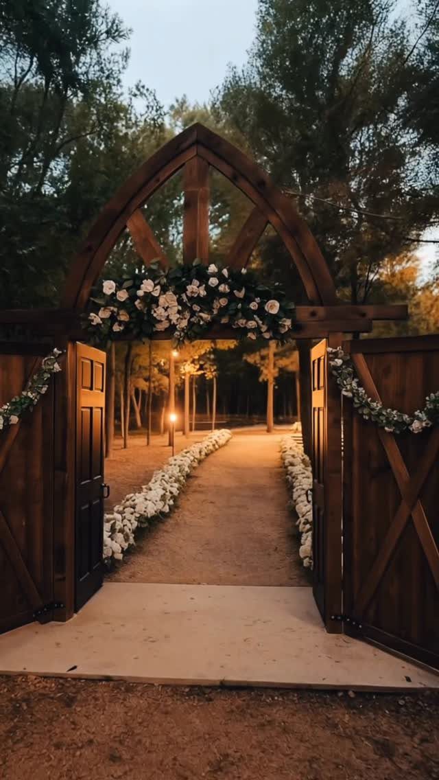 Wooden arched gateway with white flowers leading to a forest wedding ceremony path.