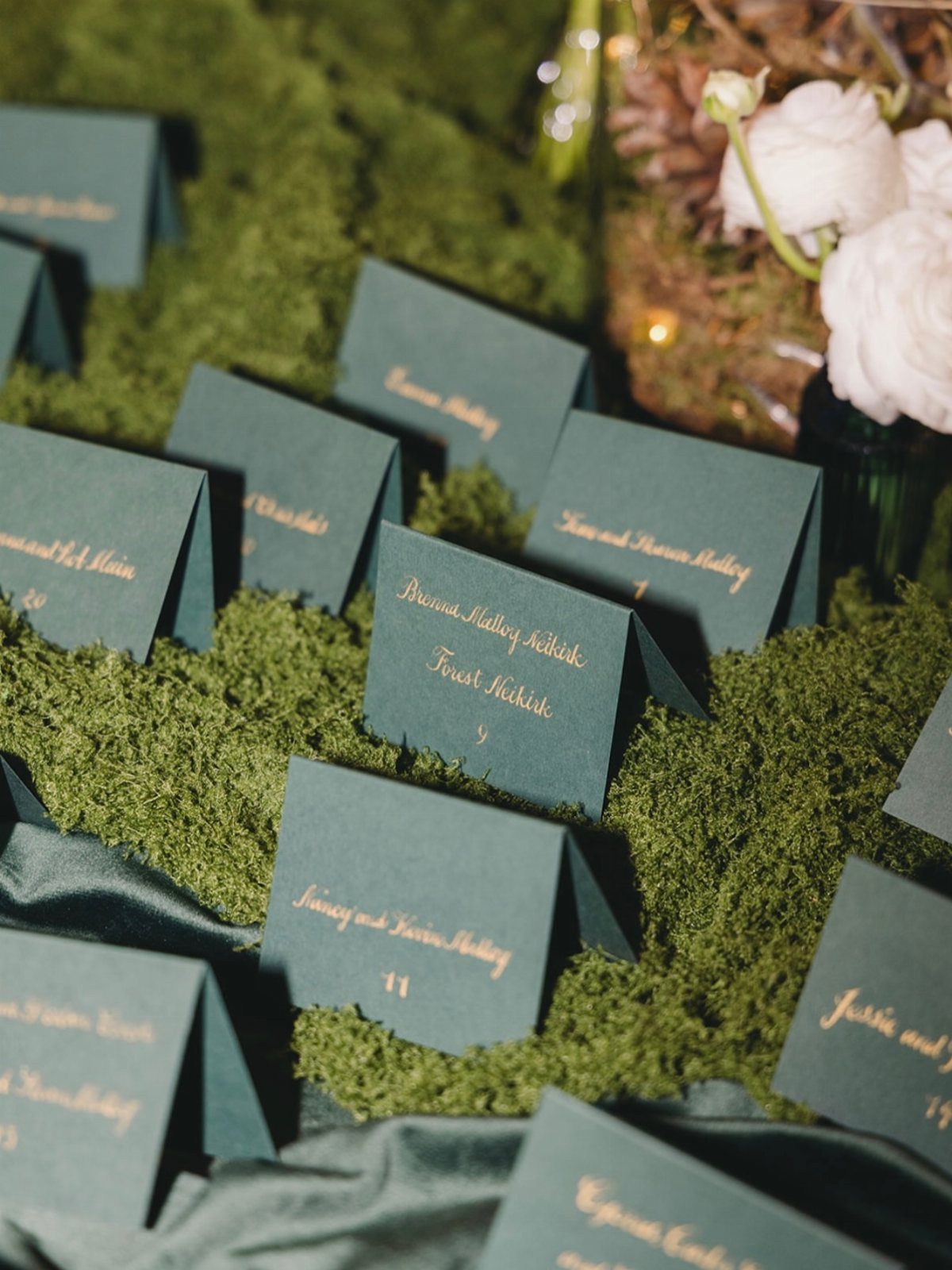 Green place cards with gold text resting on a bed of green moss.