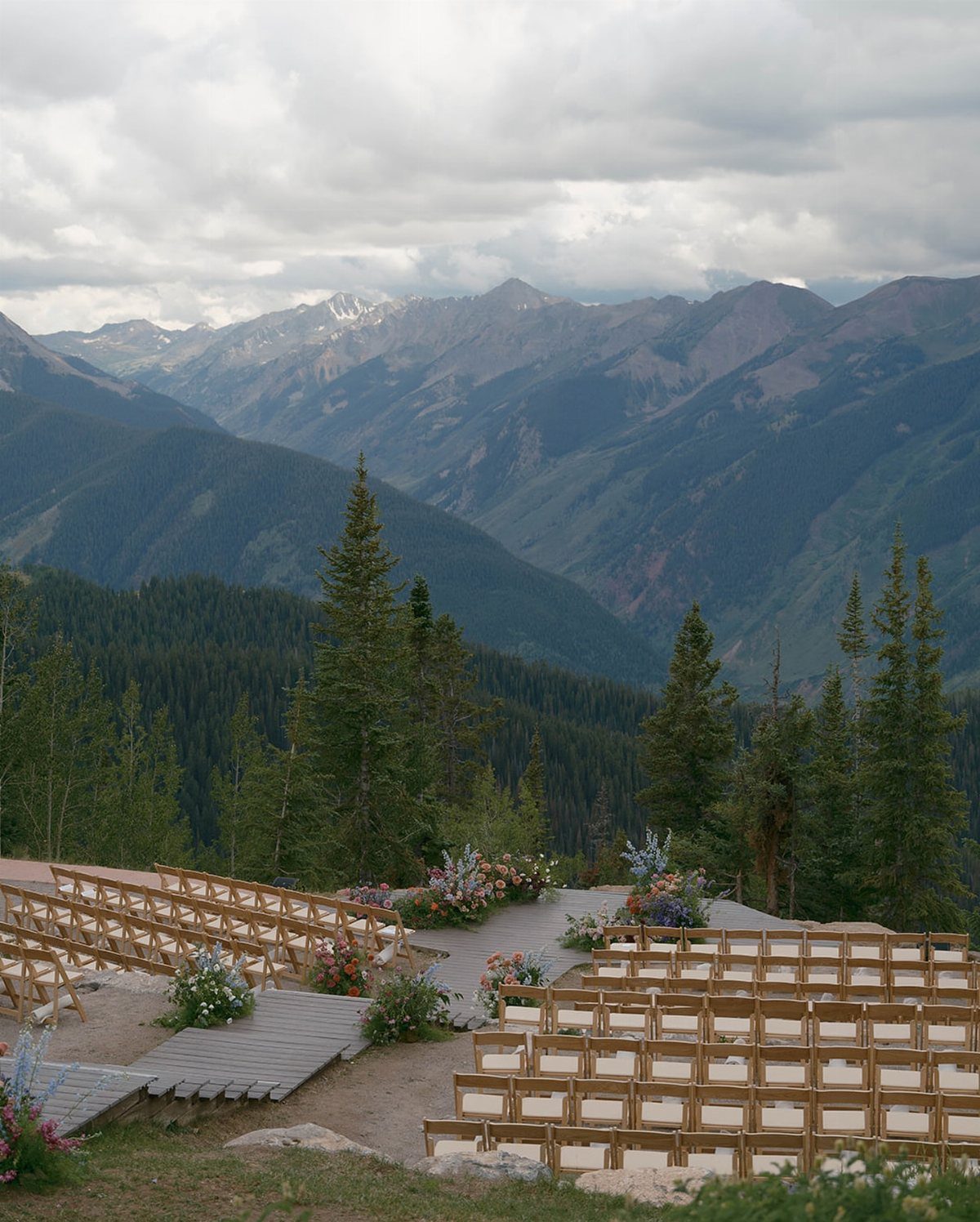 Wooden ceremony chairs and floral arrangements overlooking a forested mountain valley landscape.