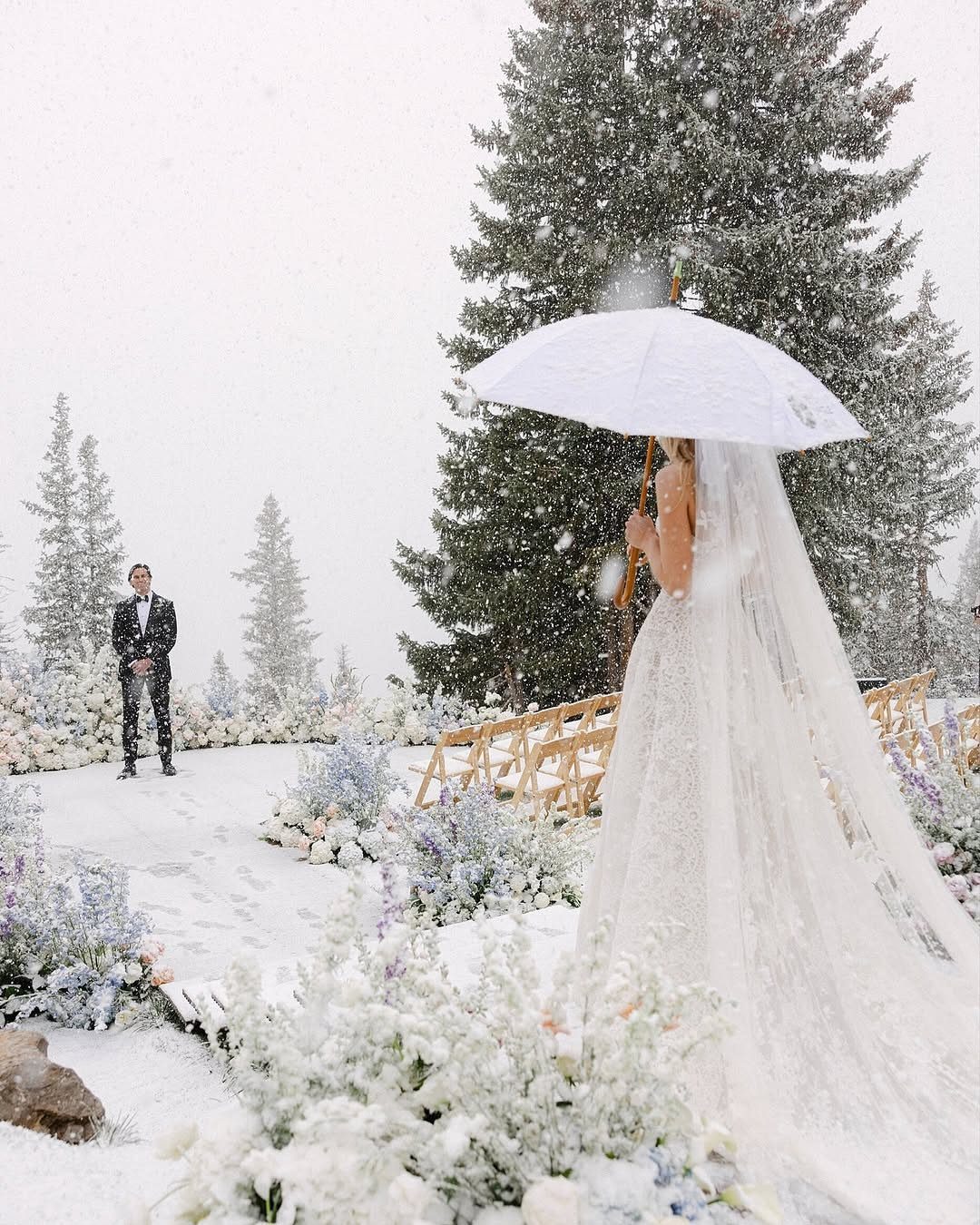 Bride with white umbrella and groom in snowy forest wedding ceremony setting