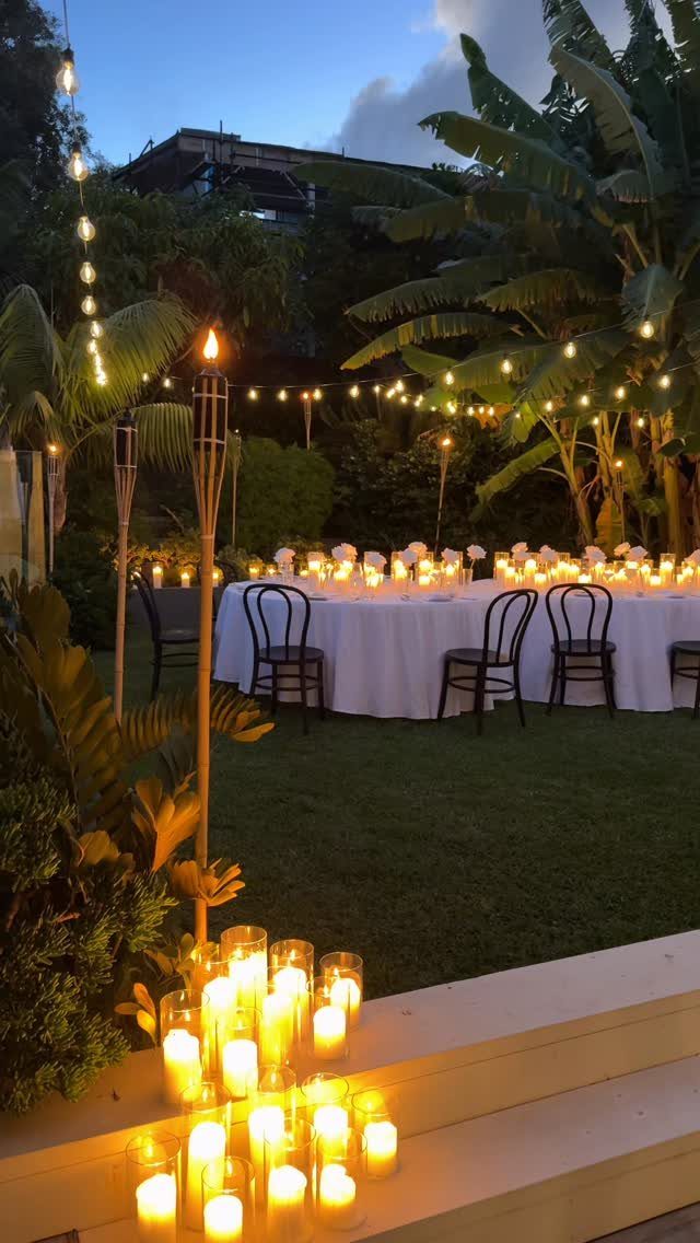 Dinner table with white cloth and black chairs in a candlelit tropical garden