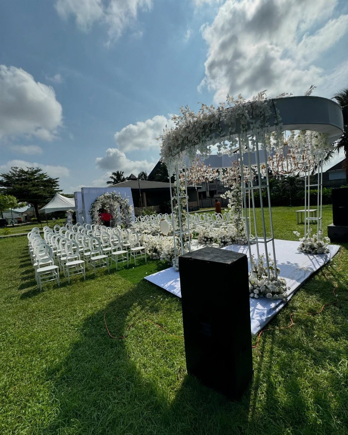 Outdoor wedding ceremony setup with white chairs and floral gazebo on green grass.