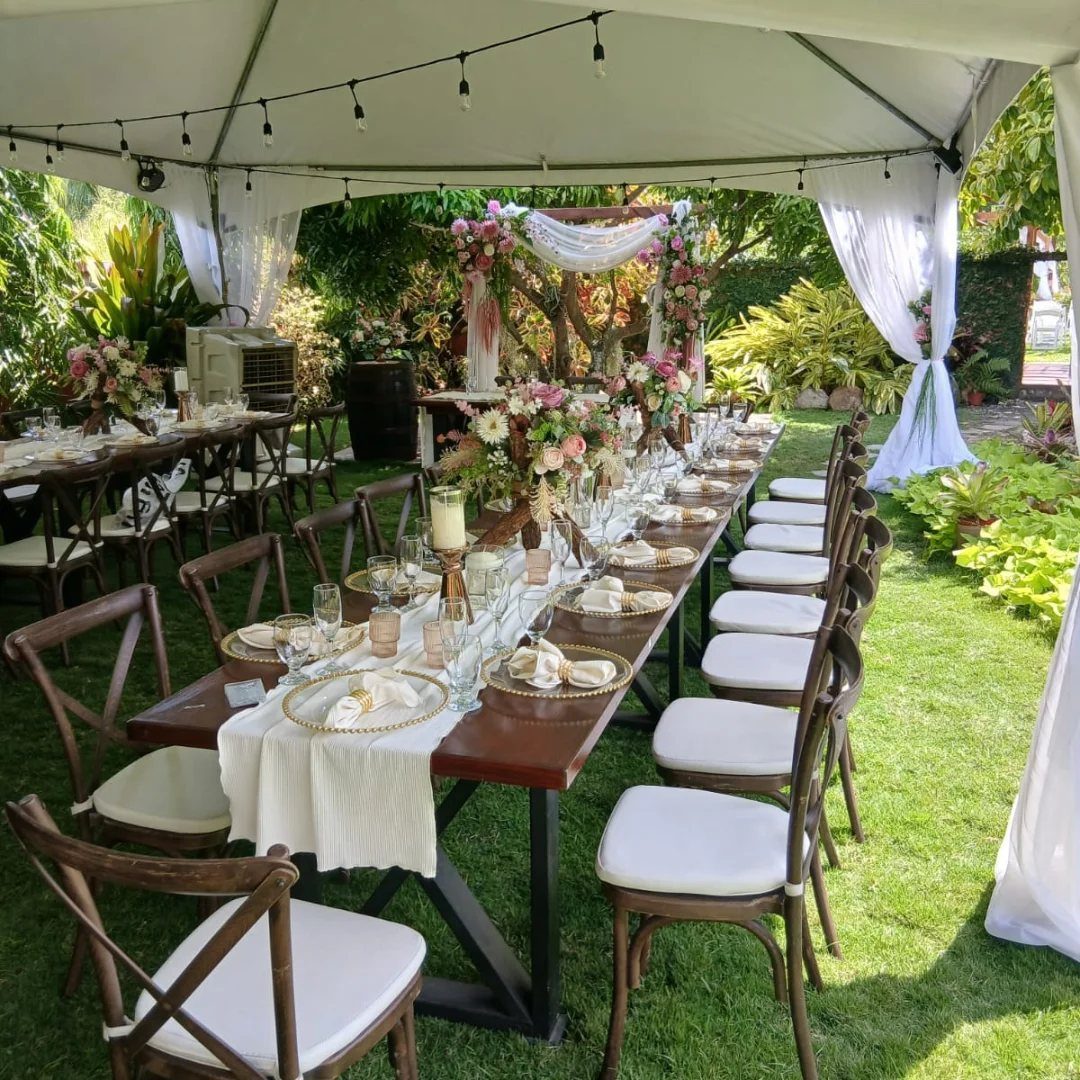 Long wooden wedding table with floral centerpieces under a white canopy tent on grass