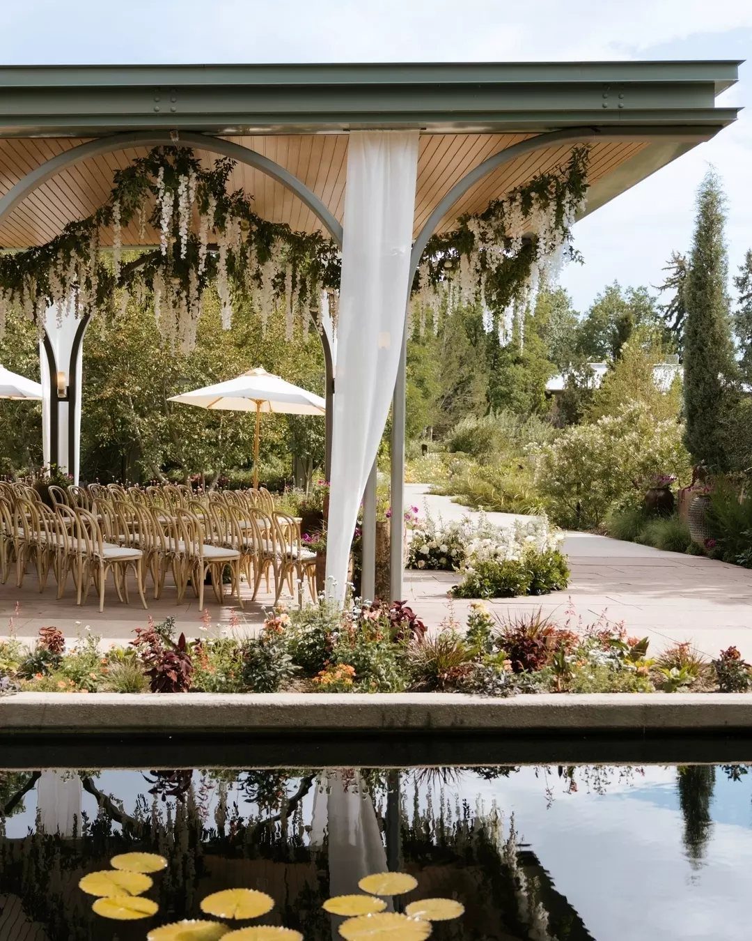 Wedding ceremony setup with gold chairs under a floral pavilion beside a lily pond
