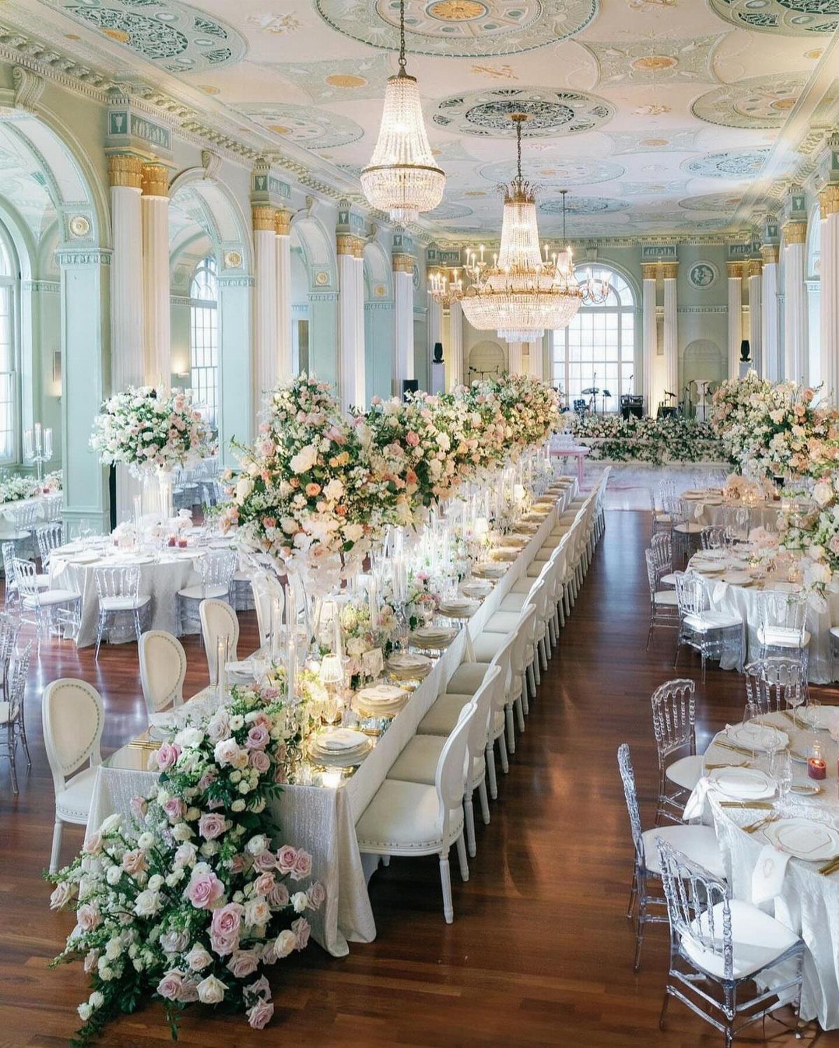 Opulent ballroom with a long banquet table decorated with abundant pink and white flowers.