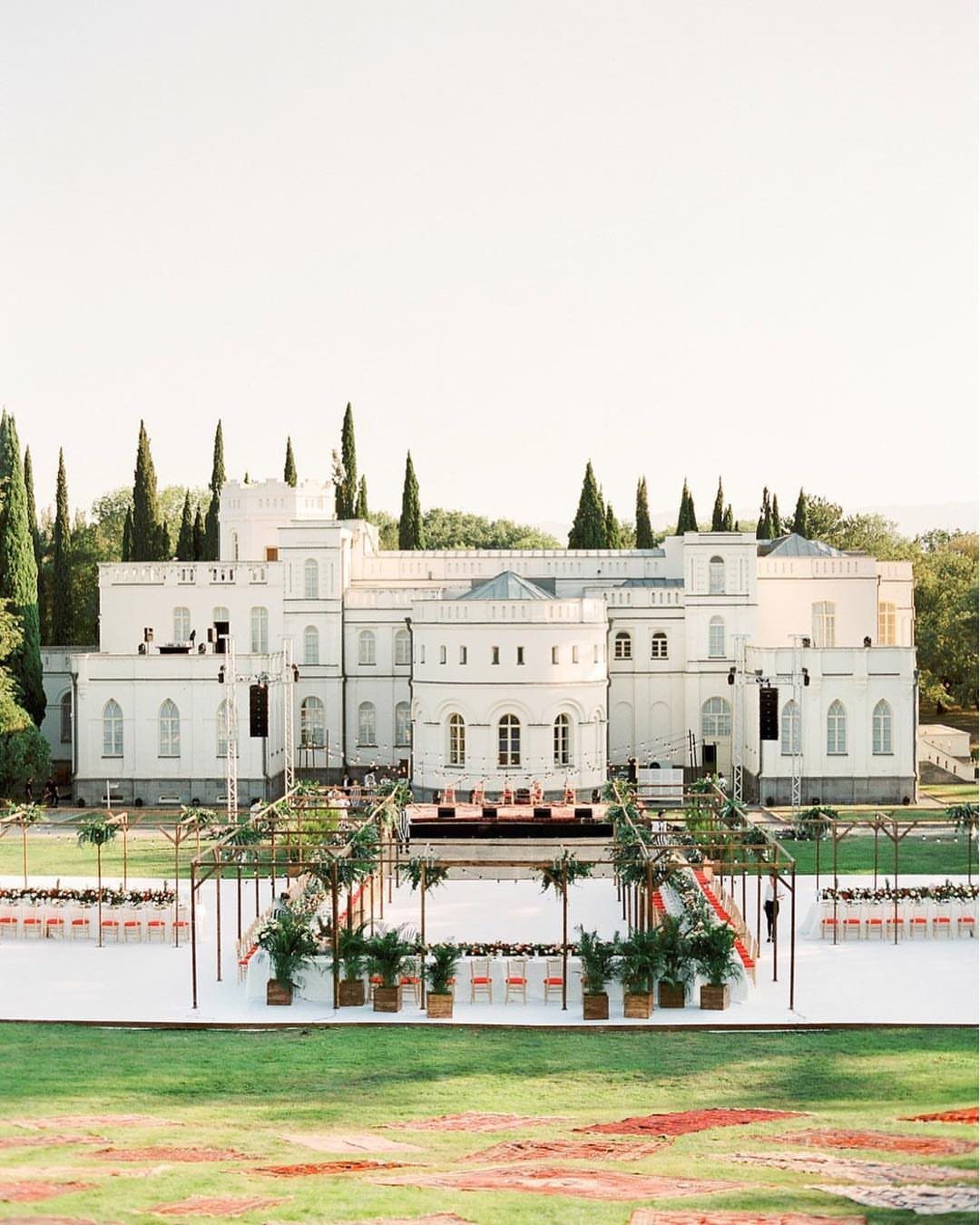 White European-style manor with an outdoor wedding ceremony setup on a green lawn.