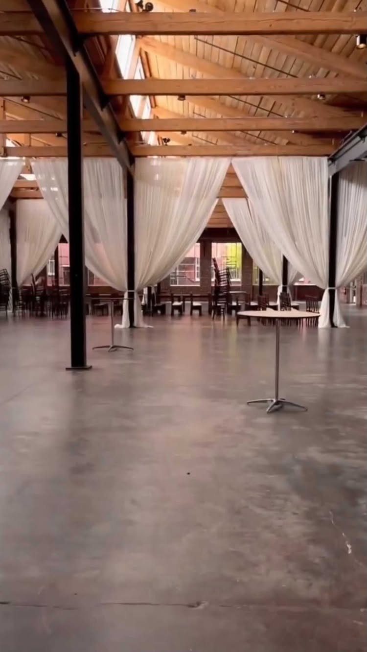 Industrial event space with polished concrete floors, wooden beams, and white fabric drapes.