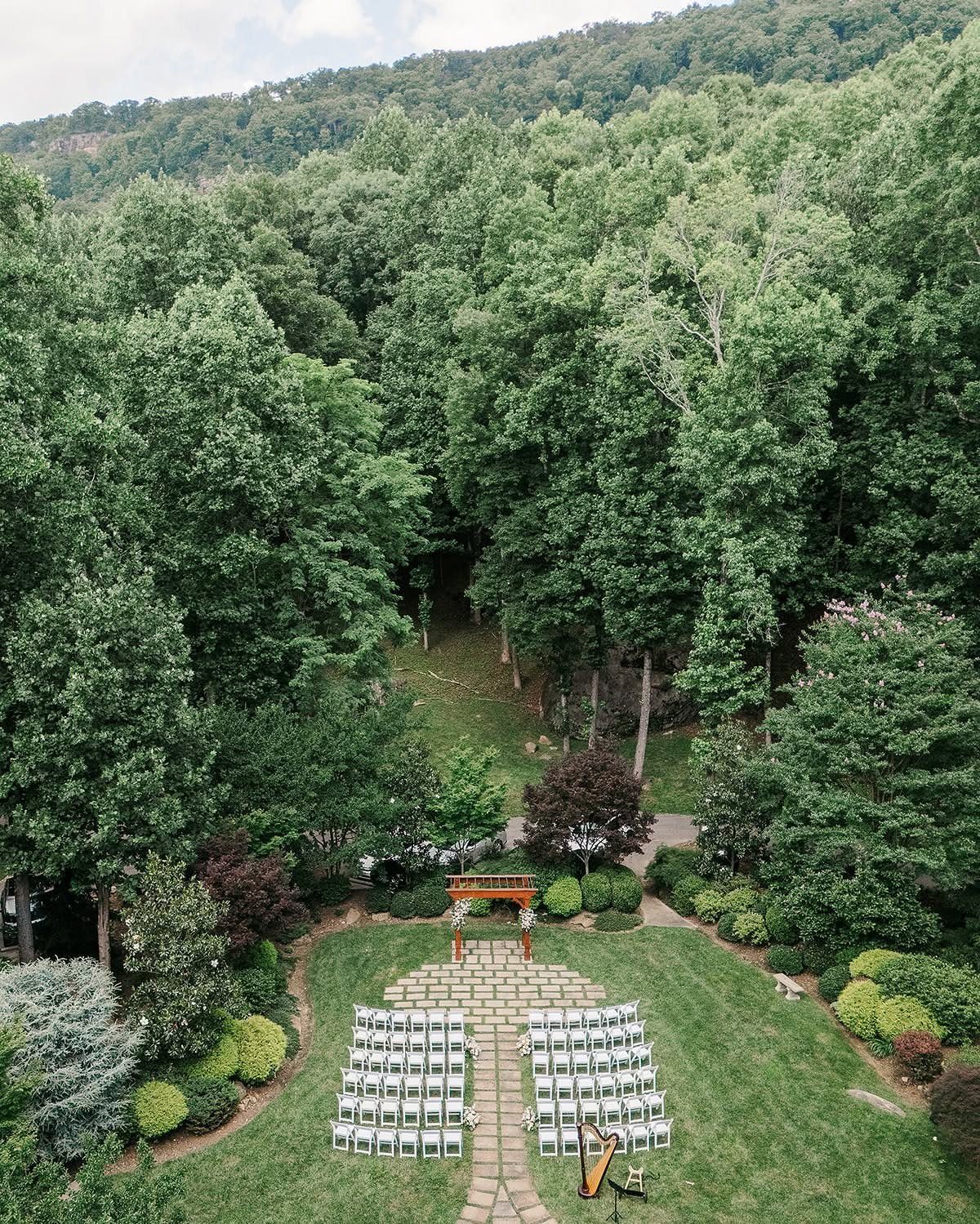 Outdoor wedding ceremony setup with white chairs and wooden arbor surrounded by forest.