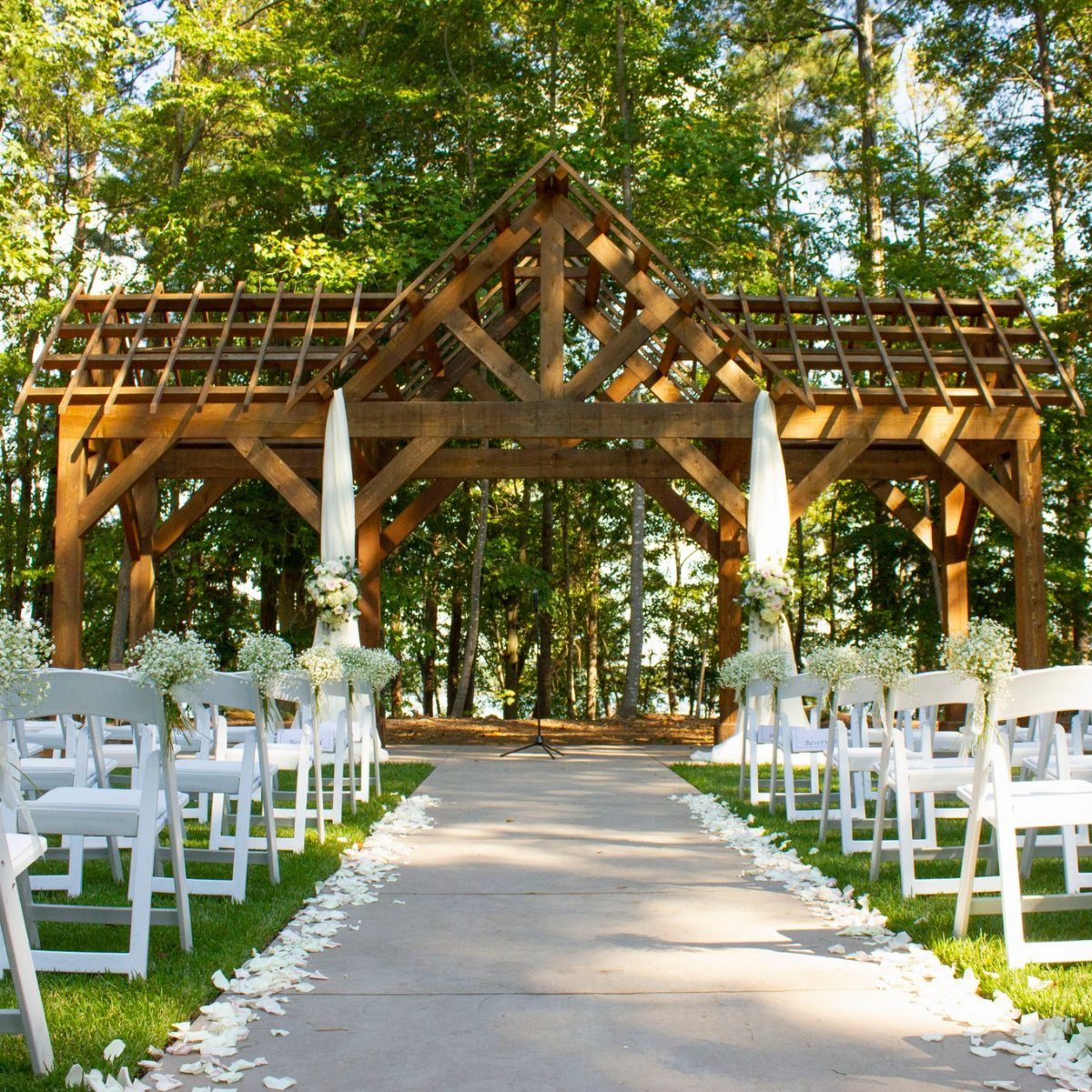 Wooden timber frame pavilion with white wedding chairs and petal-lined concrete aisle.