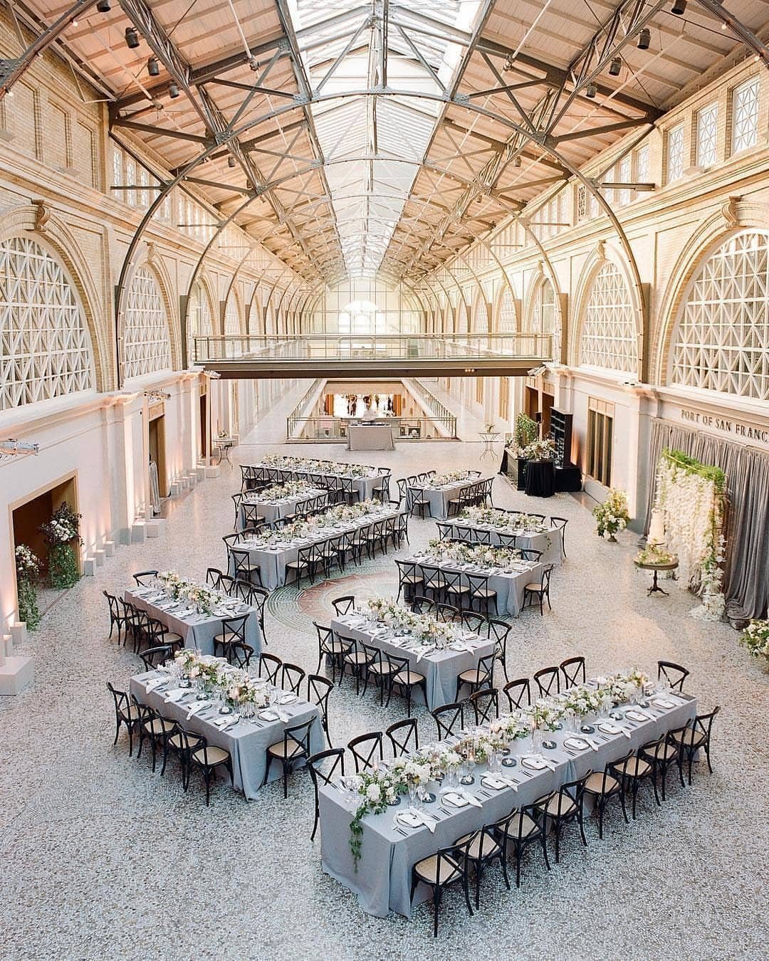 Grand indoor venue with vaulted glass ceiling and long tables set for wedding reception