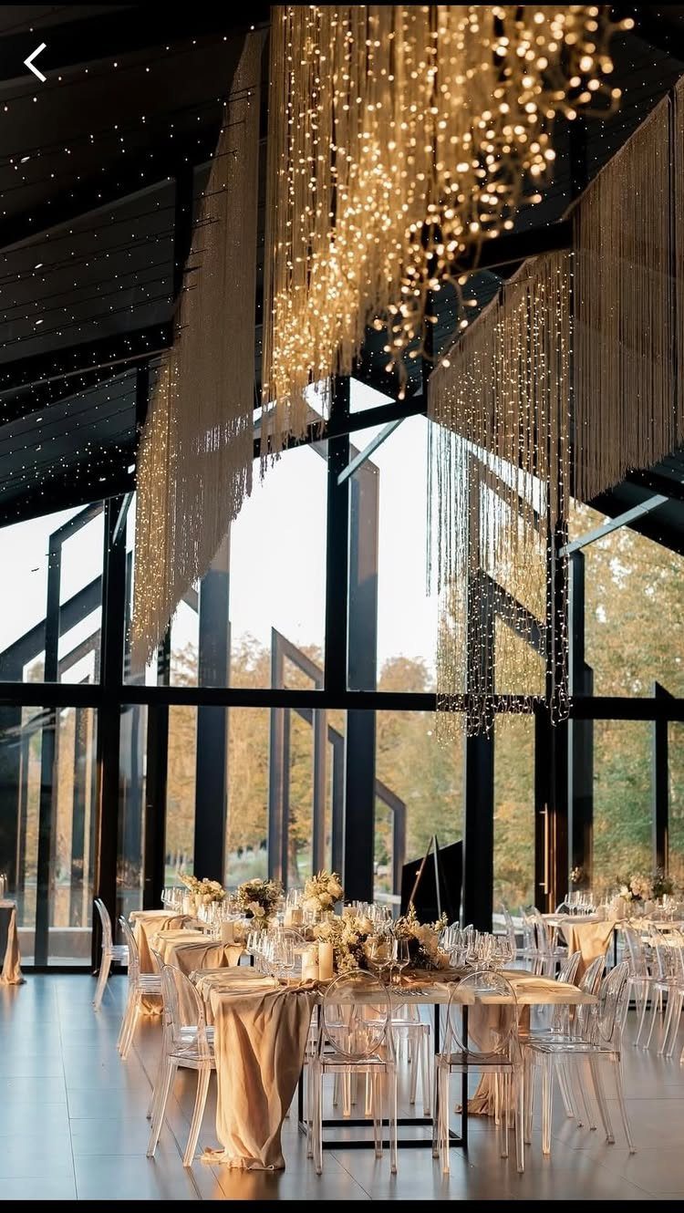 Elegant event space with golden fairy lights, clear chairs, and large windows.