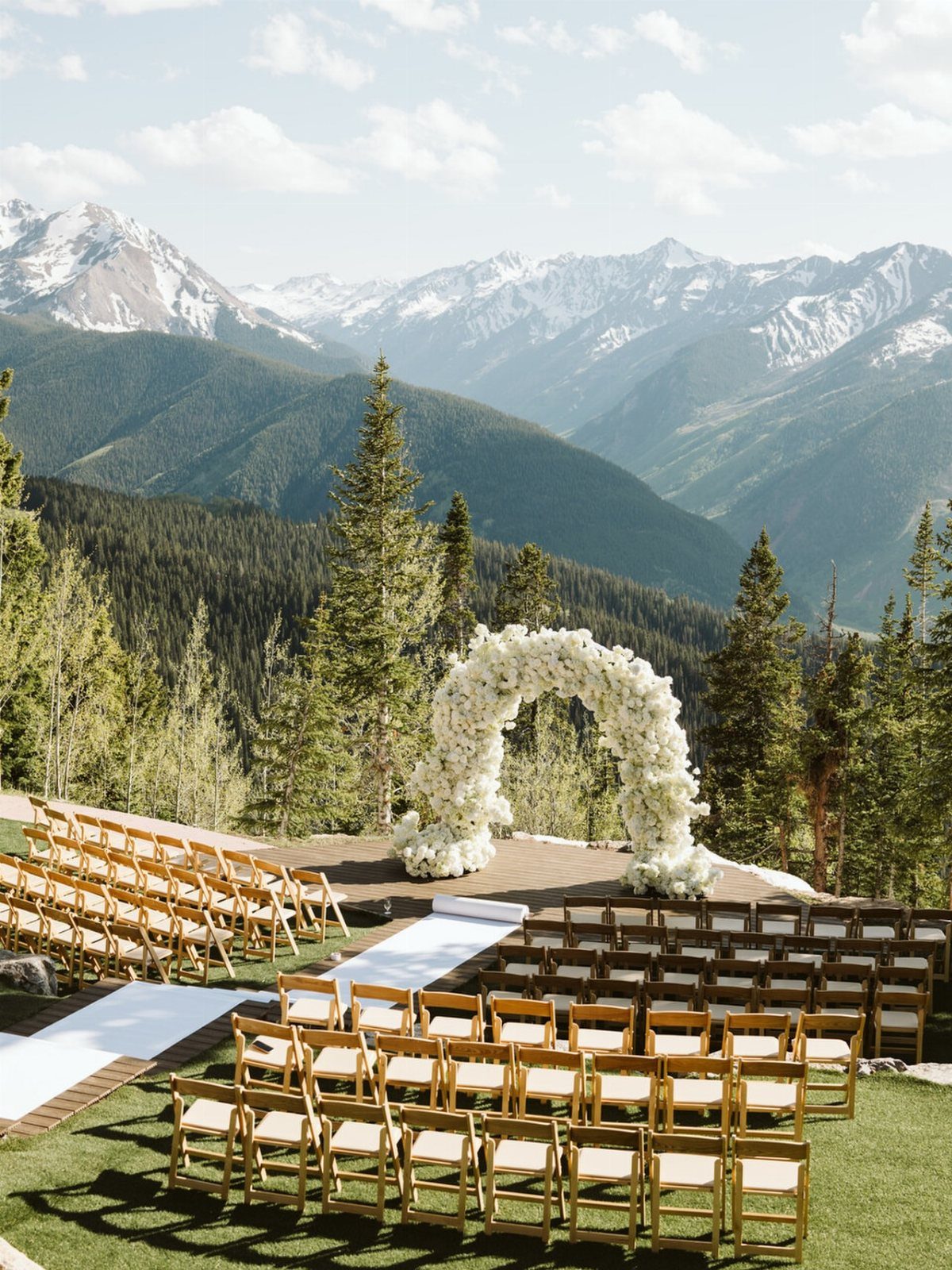 Outdoor wedding ceremony setup with a floral arch overlooking snow-capped mountain peaks.