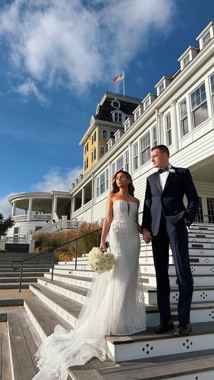 Bride and groom posing on the steps of a white seaside resort hotel.