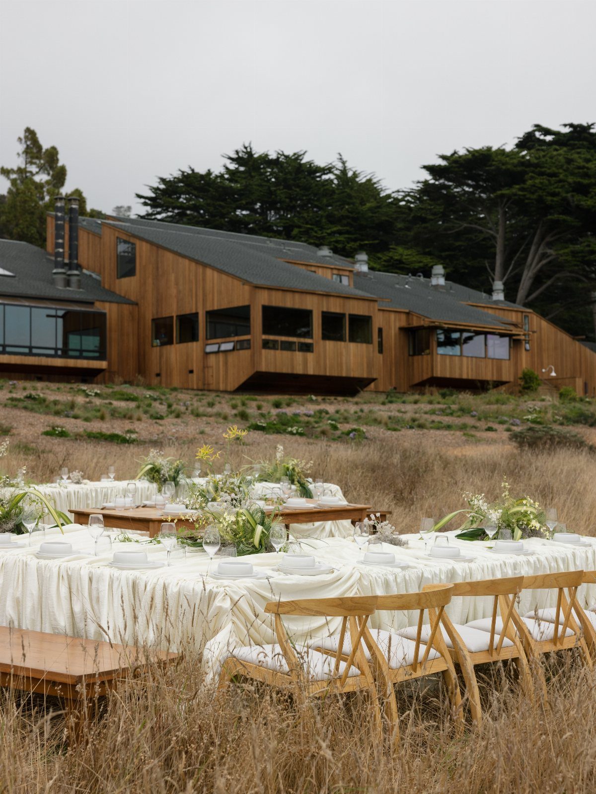 Outdoor wedding reception tables in a grassy field before a modern wooden lodge.