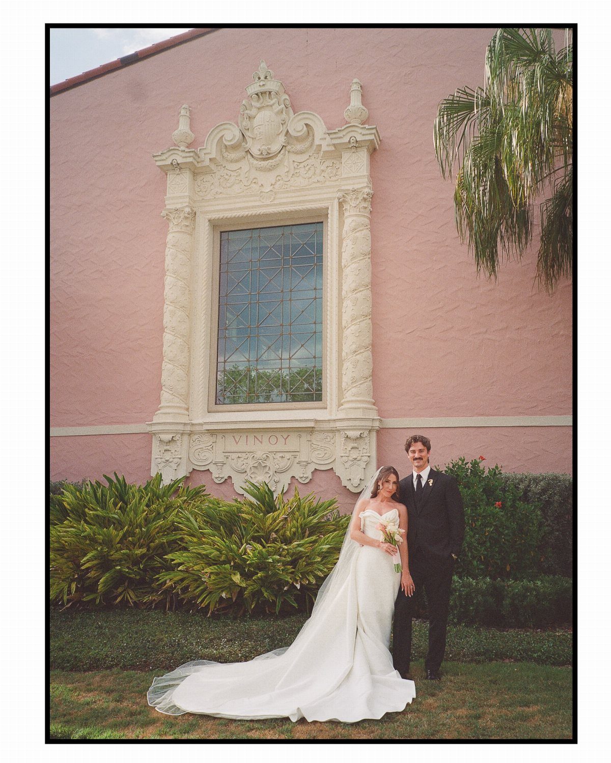 Bride and groom posing before an ornate window of the pink Vinoy hotel.