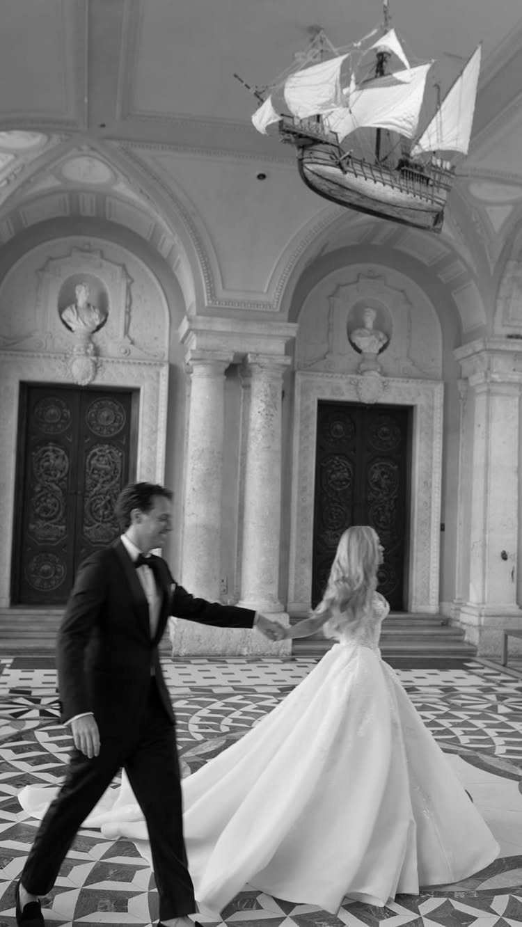 Bride and groom holding hands in a grand hall with a hanging ship.