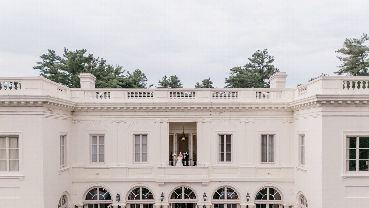 White neoclassical mansion with a bride and groom standing on a central balcony.