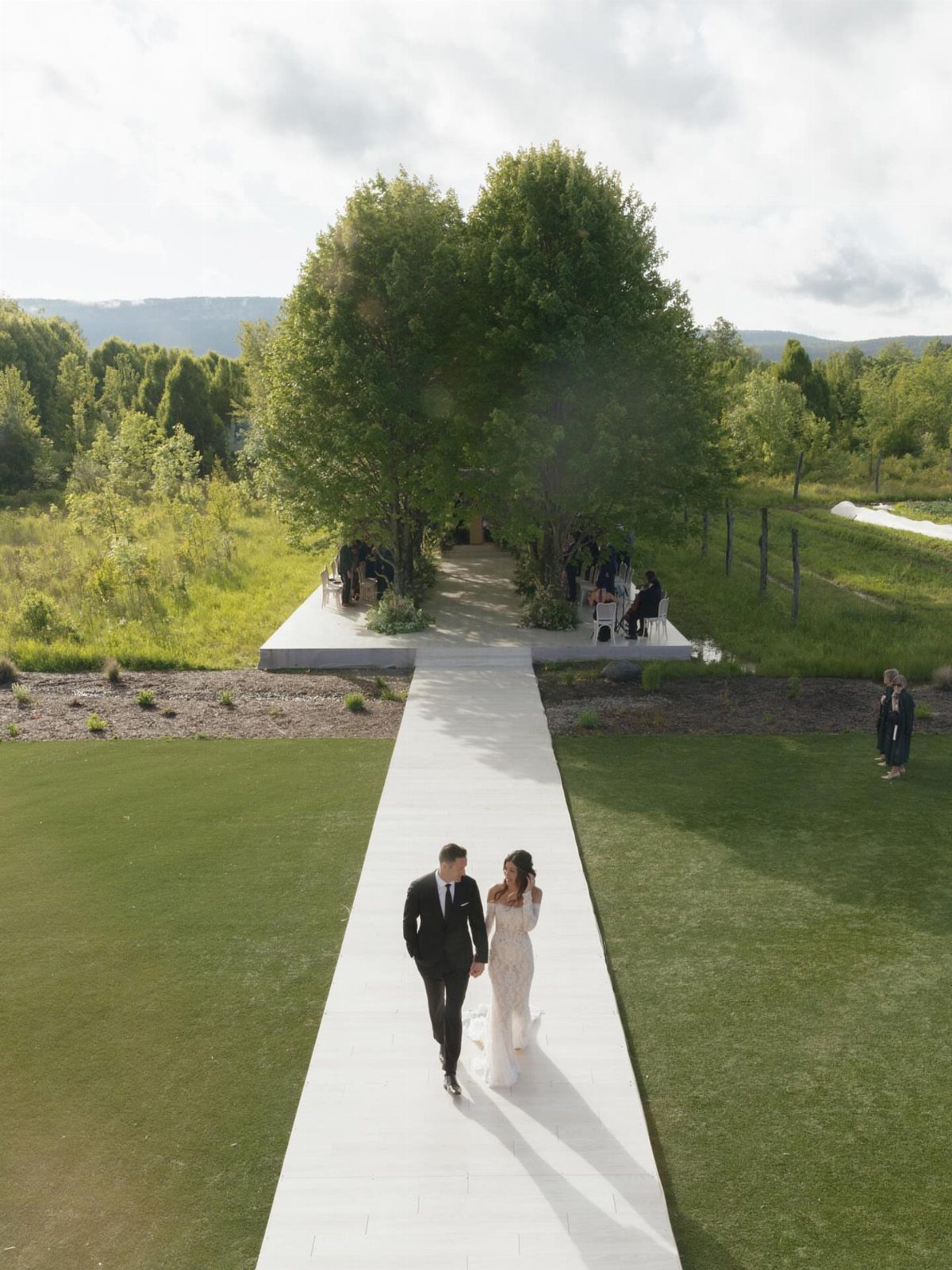 Bride and groom walking on a white stone path toward an outdoor pavilion.