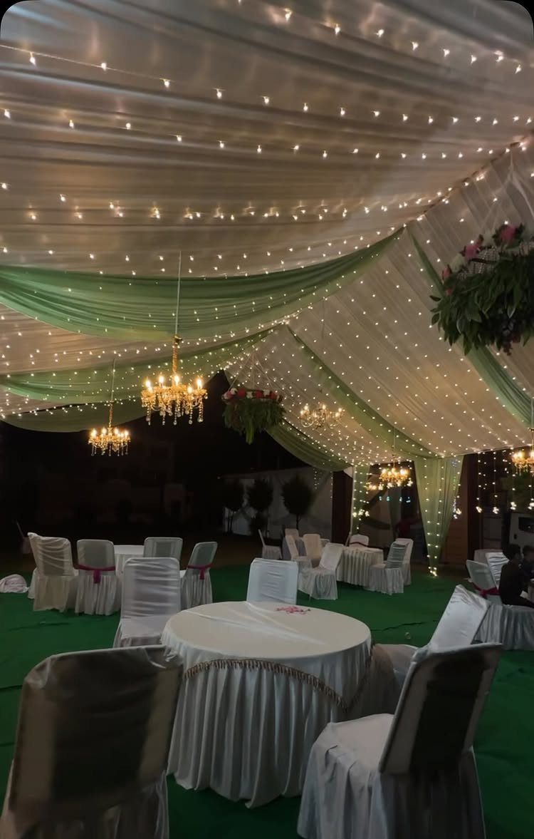 Decorated outdoor wedding venue with white and green fabric draping and chandeliers.