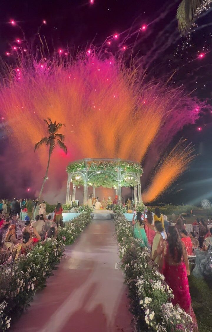Decorated wedding mandap with floral aisle and vibrant fireworks in the night sky