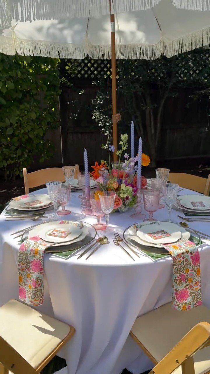 Set outdoor dining table with floral napkins and centerpiece under a white umbrella.