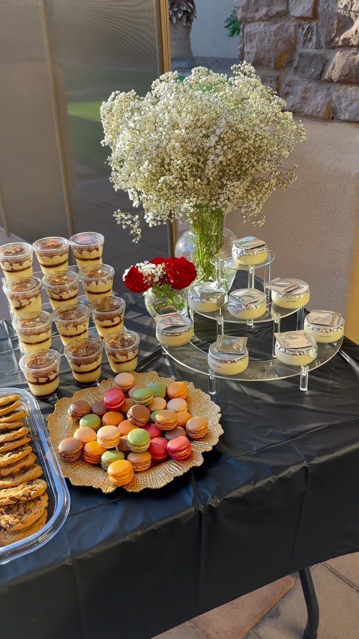 Dessert table with colorful macarons, mini cakes, layered cups, and white baby's breath.