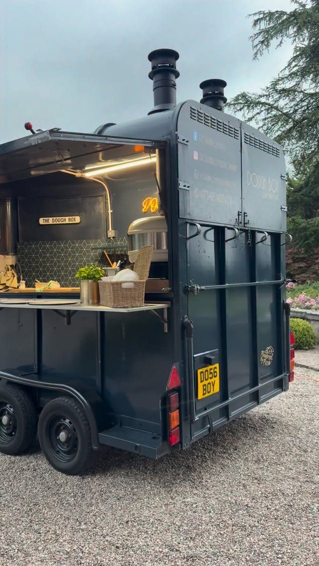 Black mobile food truck with open serving window parked on a gravel driveway
