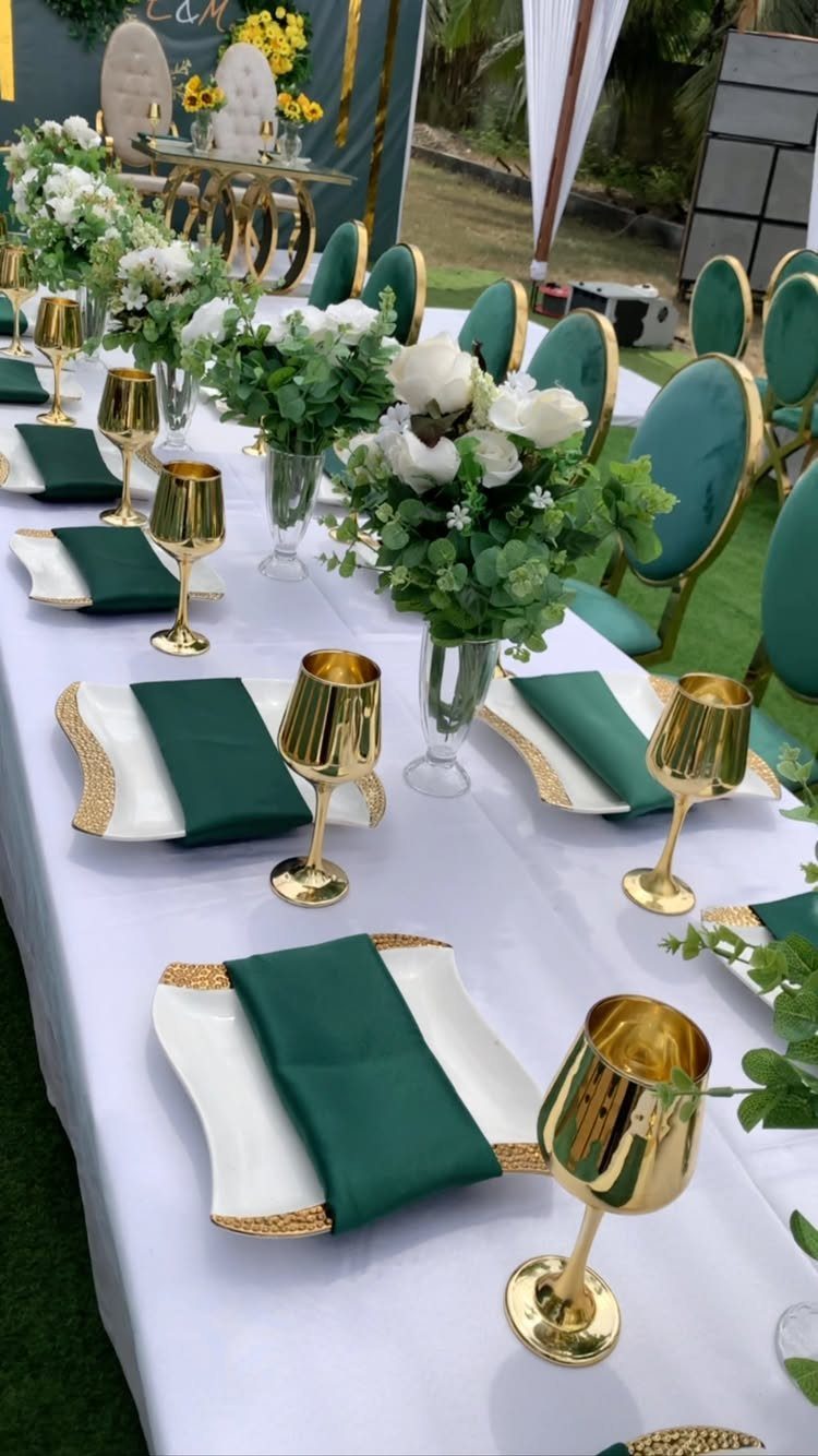 Wedding table setting with white roses and greenery centerpieces, gold goblets, and green napkins.
