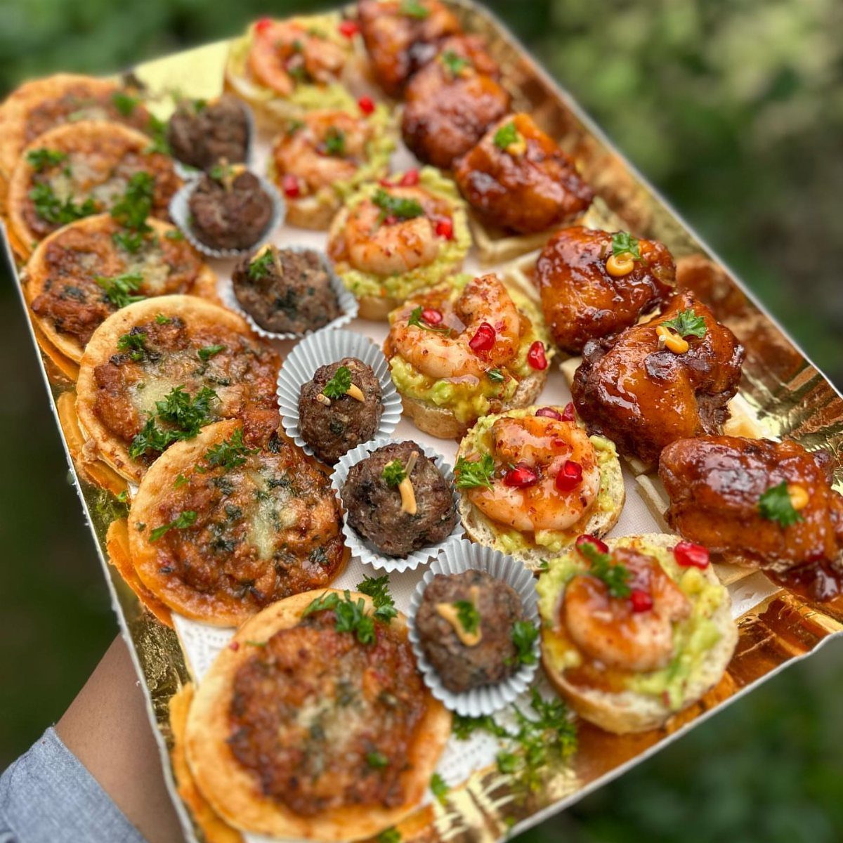 Assorted appetizers on a gold tray including mini quiches, shrimp, and meatballs.