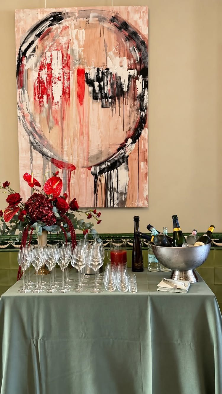Champagne glasses and wine bottles on a green table with red floral arrangements.