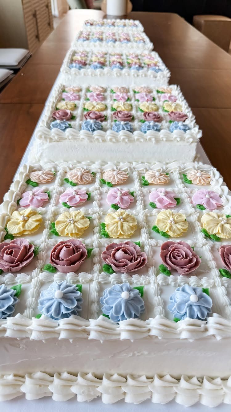Long white wedding cake decorated with colorful buttercream frosting flowers on a table