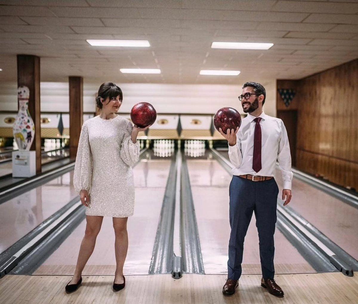 Couple in wedding attire holding bowling balls on a bowling alley lane