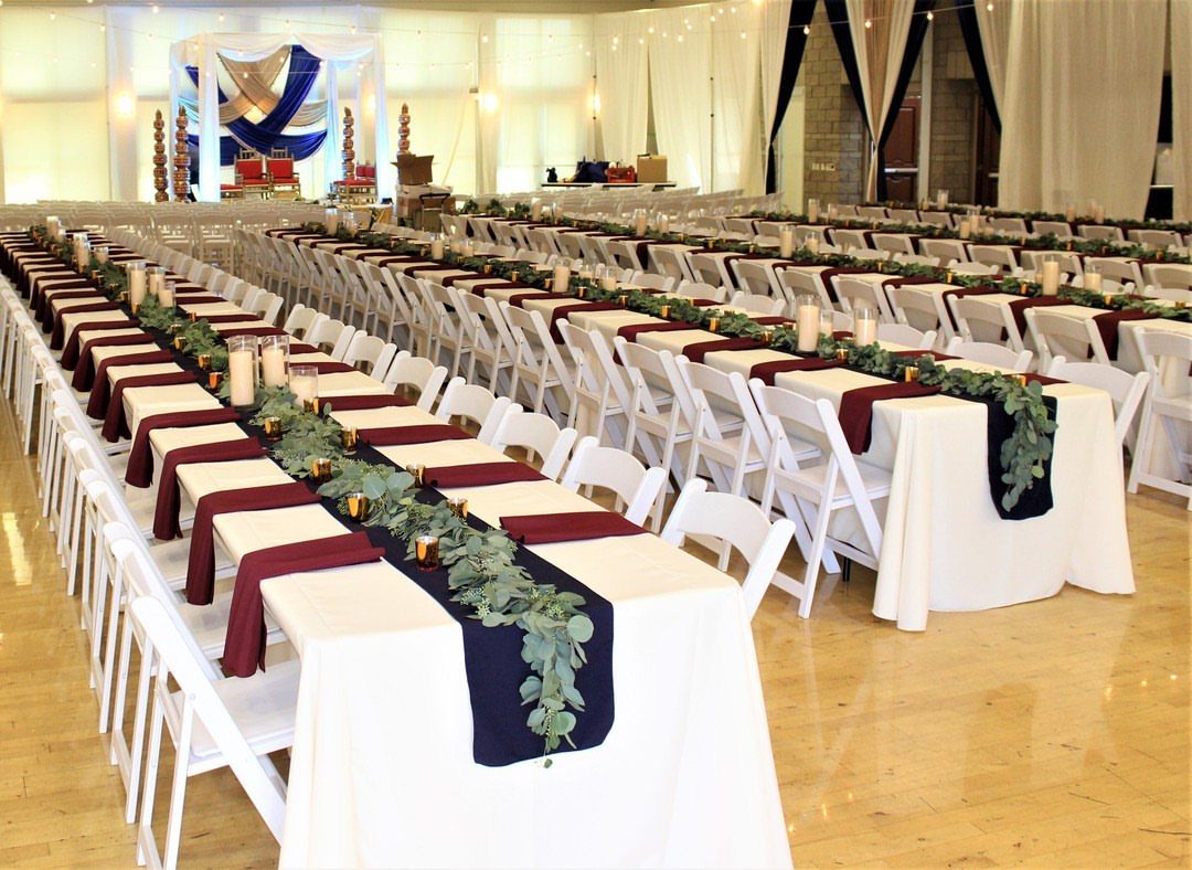 Banquet tables with white cloths and greenery in a large community hall setting.