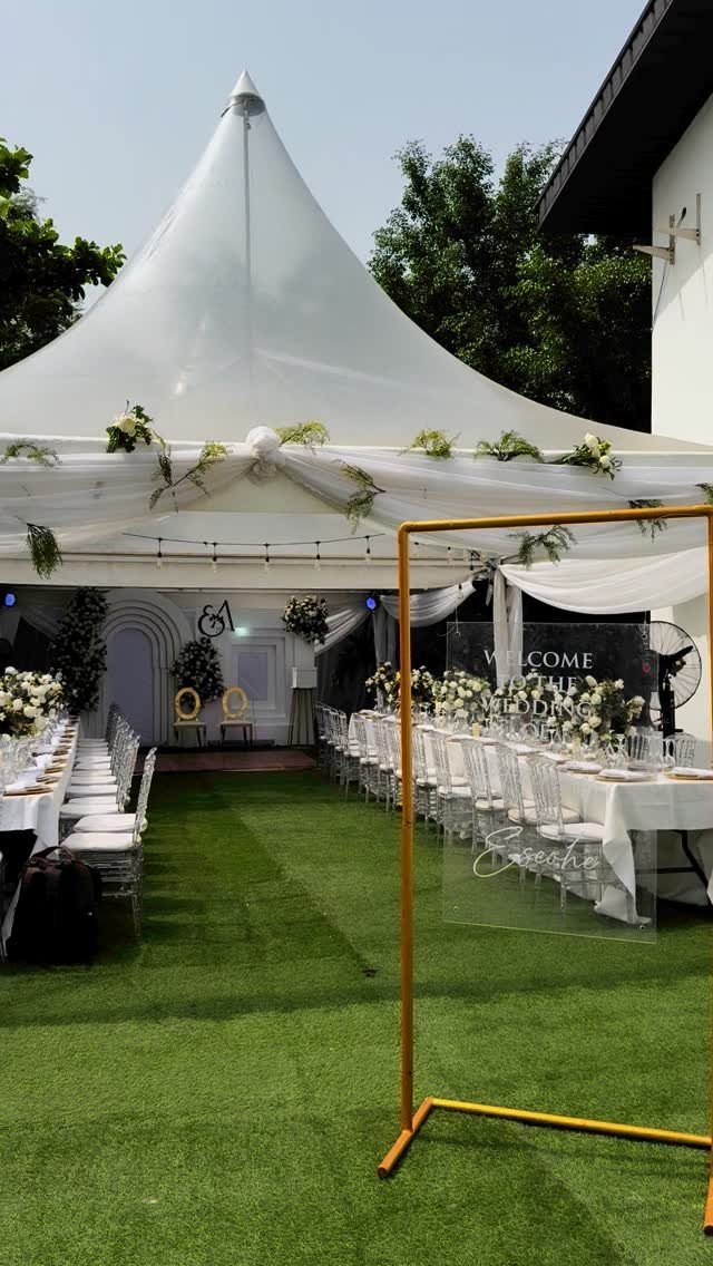 Outdoor wedding reception with white tables and chairs under a large white tent.