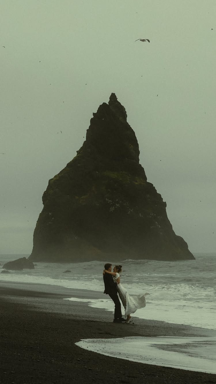 Wedding couple embracing on a black sand beach before a massive sea stack.