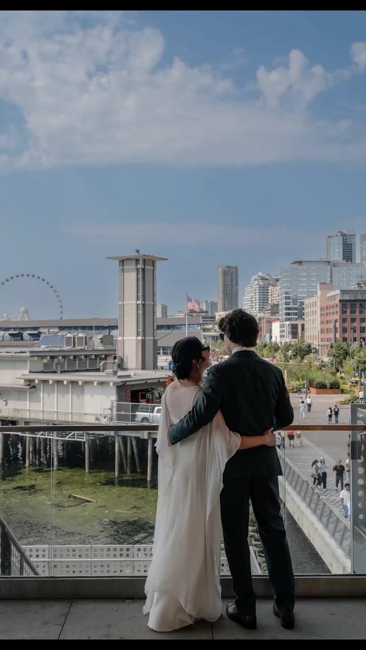 Couple in wedding attire overlooking the Seattle waterfront and city skyline from a balcony.