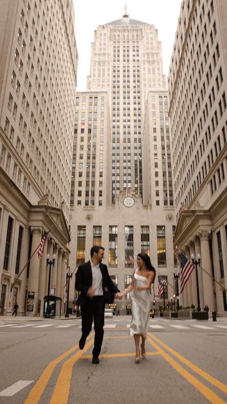 Newlywed couple walking hand in hand across a city street between tall skyscrapers.