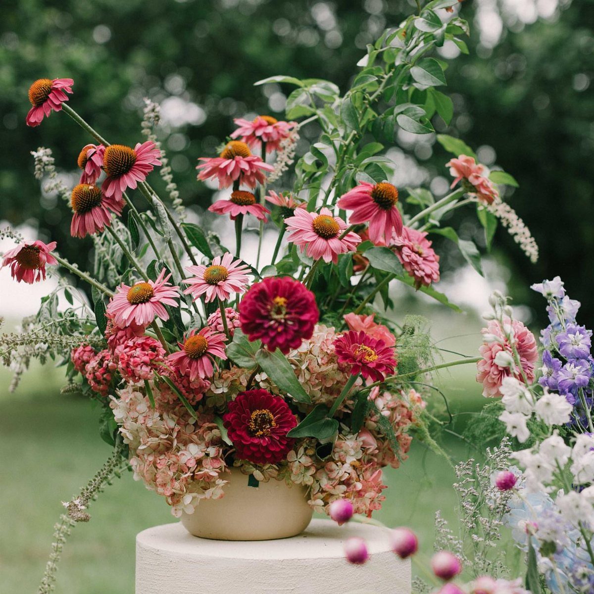 Colorful floral arrangement with pink coneflowers and red zinnias on a white pedestal.