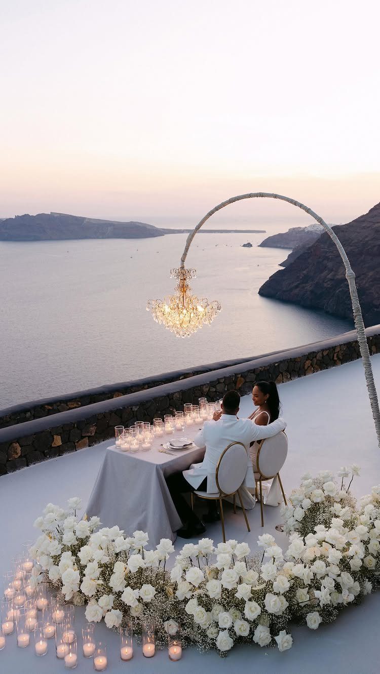 Couple in wedding attire dining at a romantic table with white roses and chandelier.
