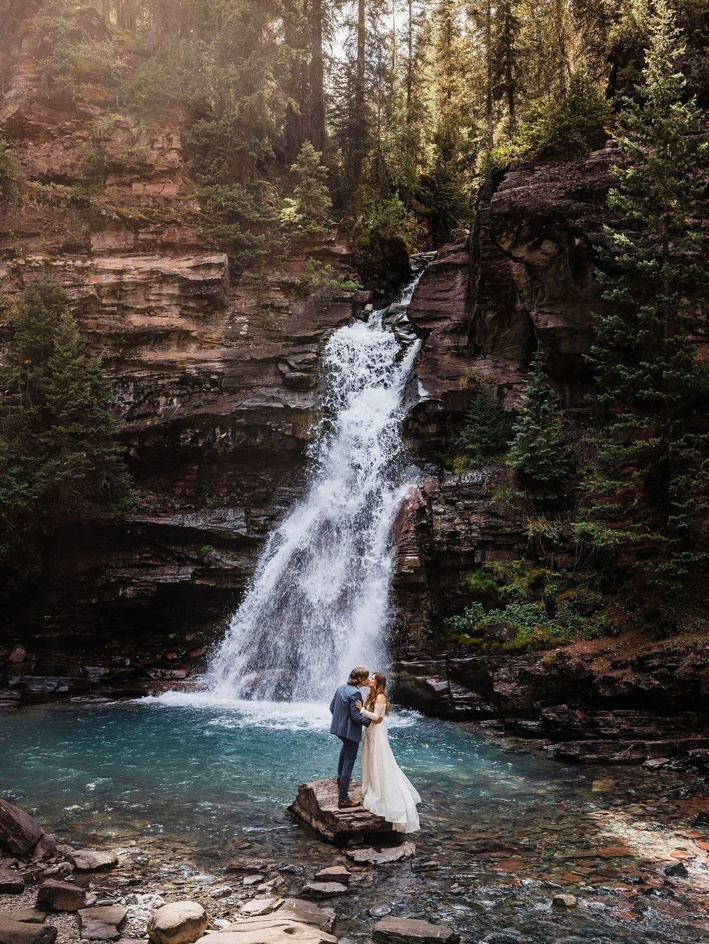 Wedding couple embracing on a rock before a waterfall in a mountain forest.