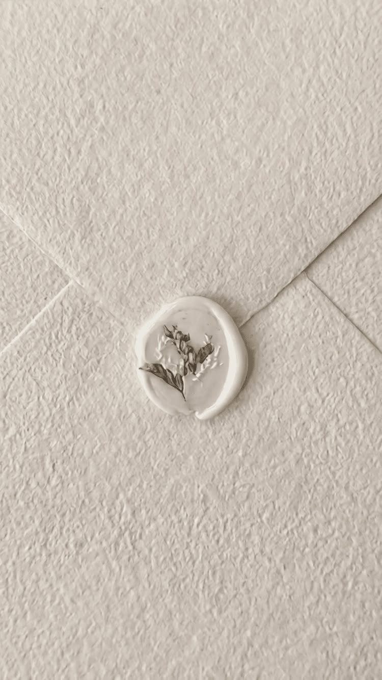 Cream textured envelope sealed with a white wax seal and dried flower sprig