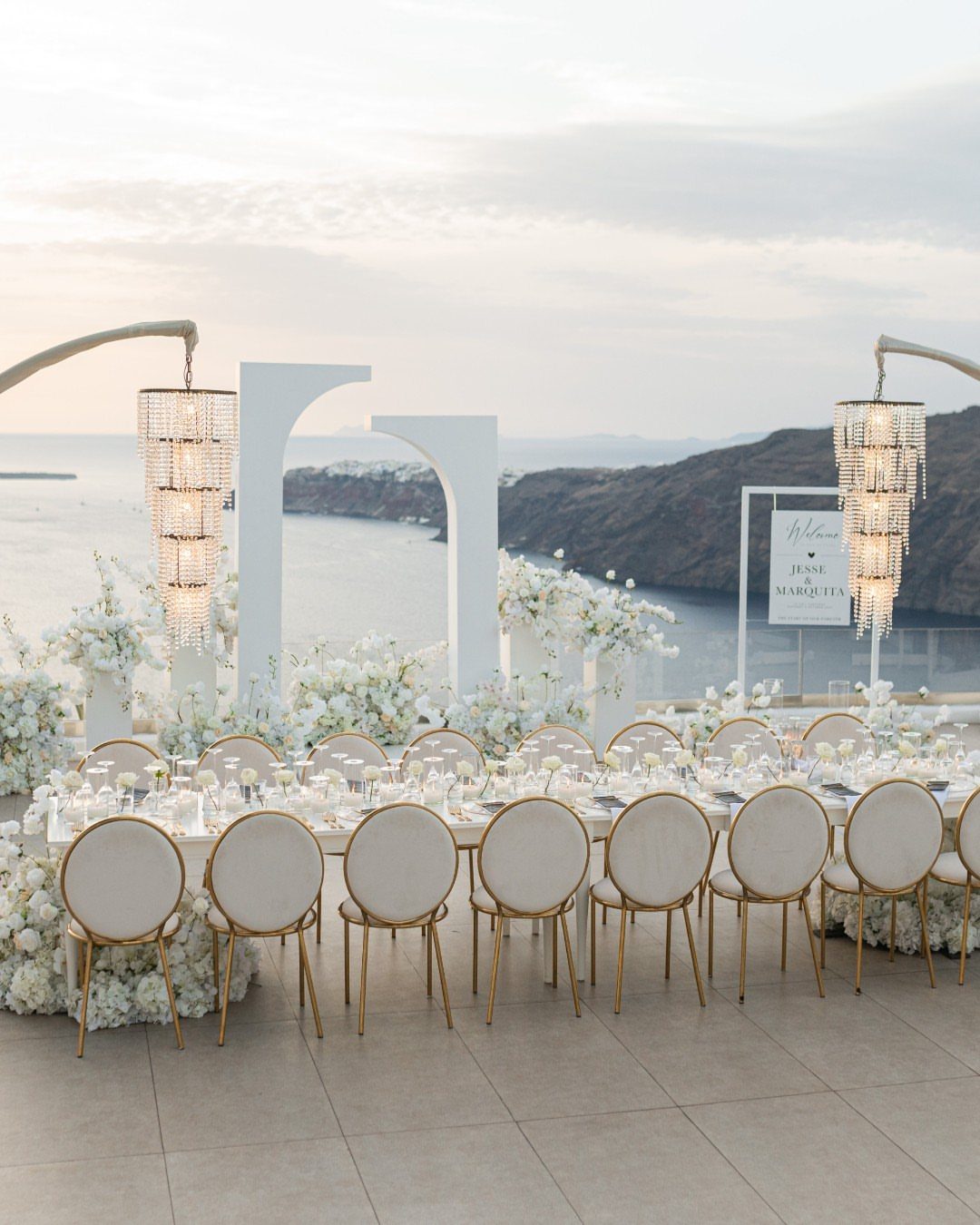 Elegant outdoor wedding reception table with white flowers and crystal chandeliers overlooking the sea